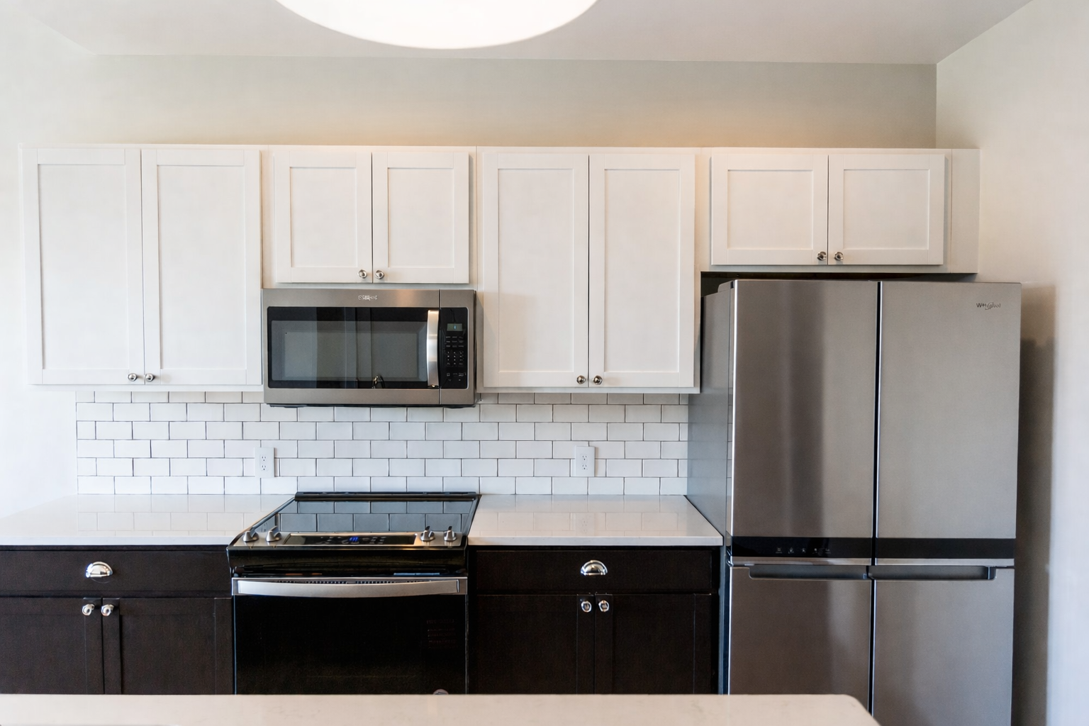 Modern urban apartment kitchen featuring stainless steel appliances white shaker cabinets subway tile backsplash and quartz countertops